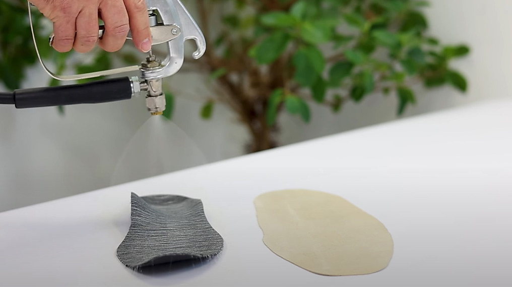 Sprühpistole besprüht Schuheinlagen, die auf einer Tischplatte liegen